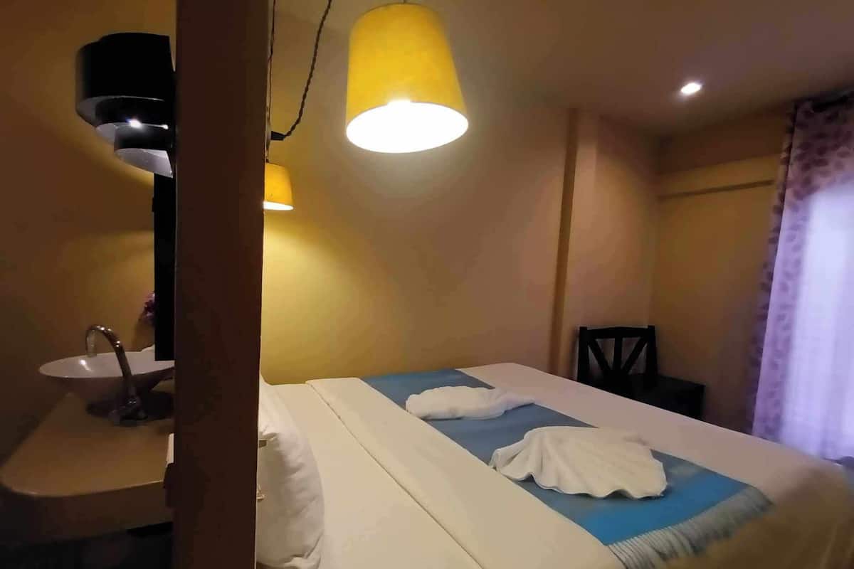 Una habitación de hotel con una cama, una mesita de noche, un lavamanos y un espejo.