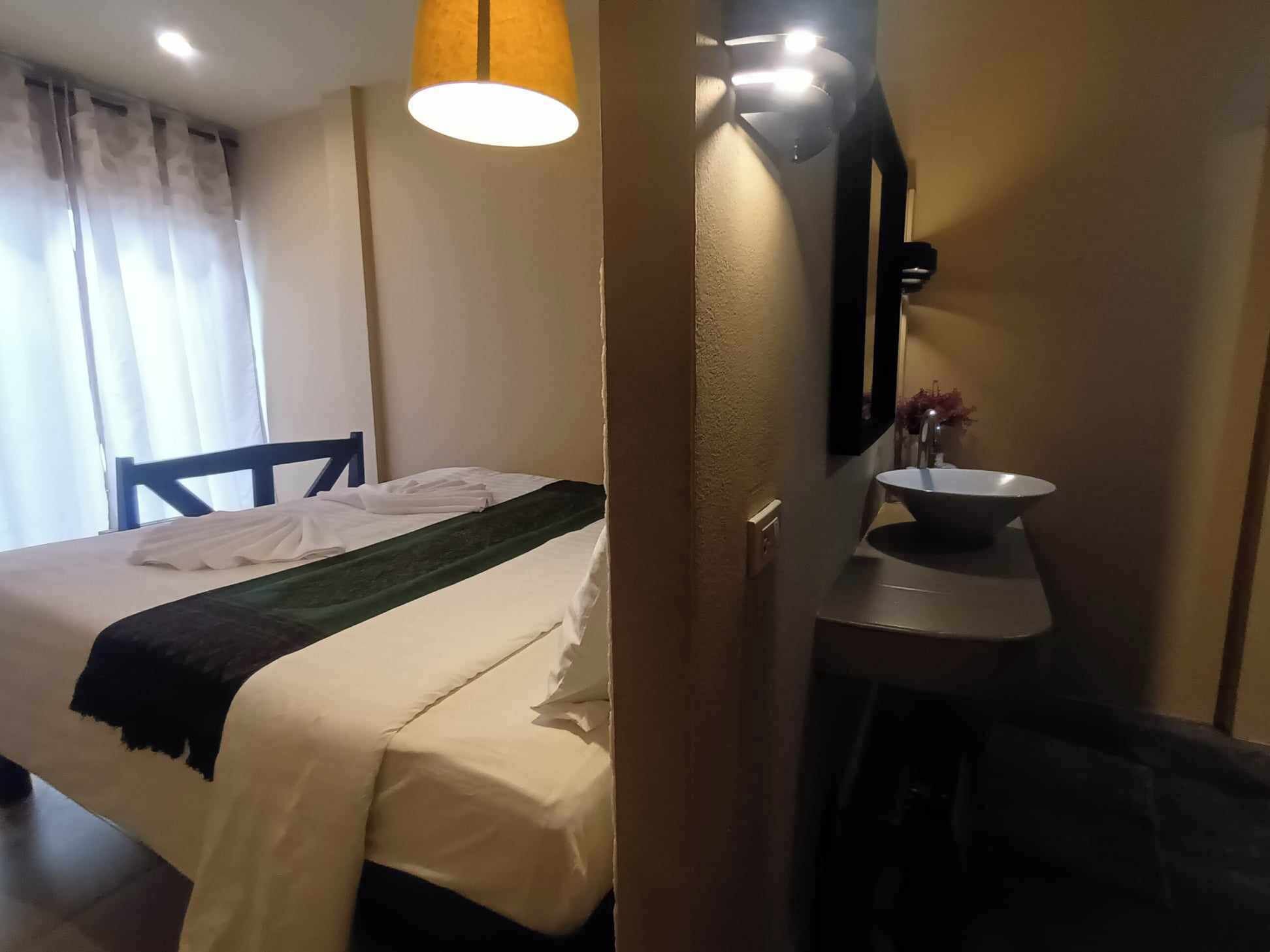 Una habitación de hotel con cama, una mesita de noche con lavamanos y un espejo.