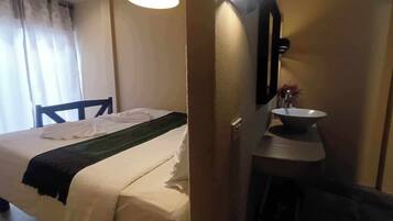 Una habitación de hotel con cama, una mesita de noche con lavamanos y un espejo.