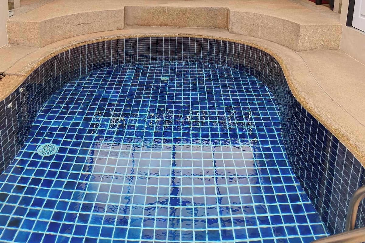 Una piscina con azulejos azules, rodeada por una zona cubierta con ventilador de techo, pared de bambú y asientos.