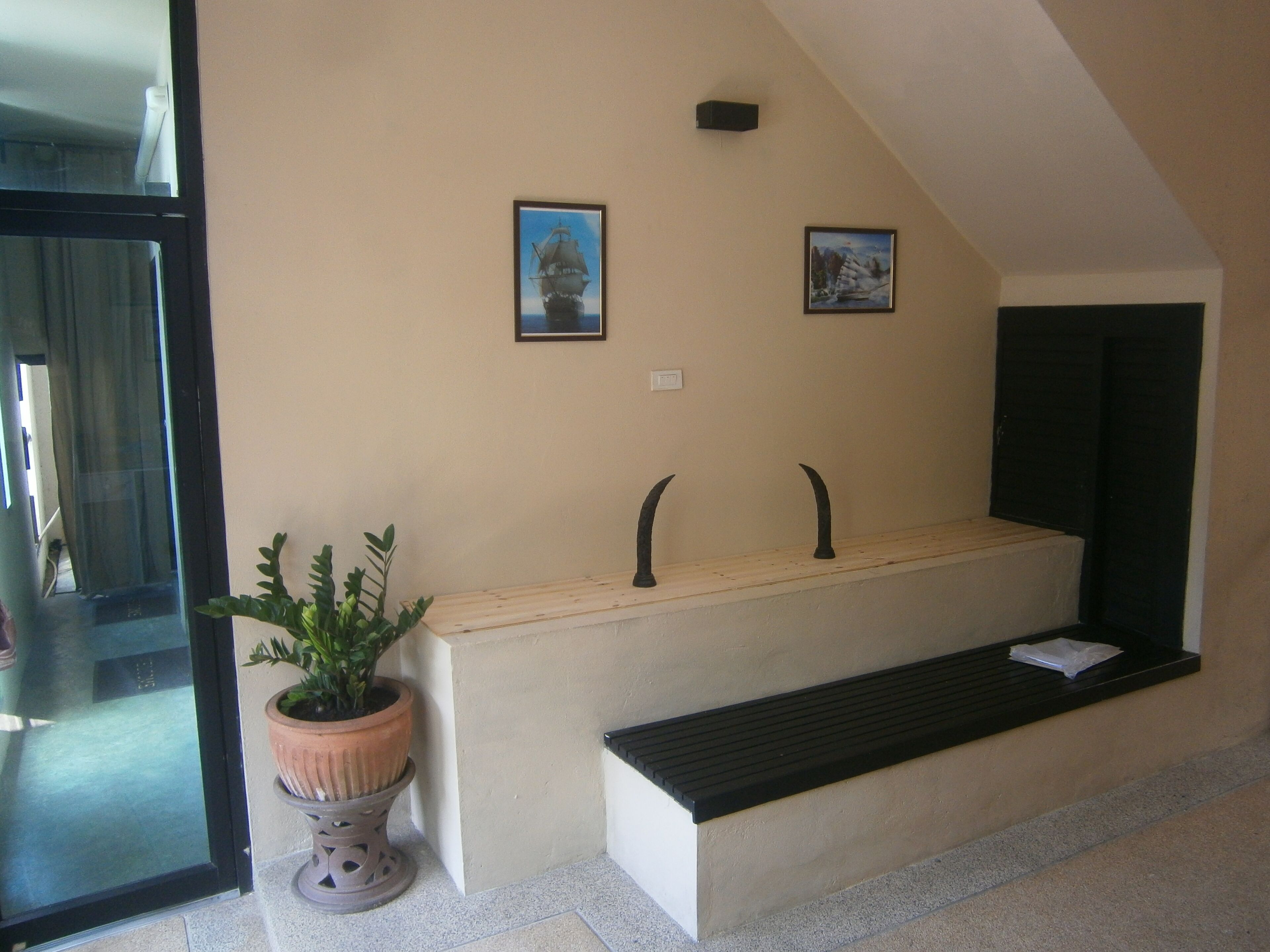 A reception area with a bench, a potted plant, and two framed pictures on the wall.