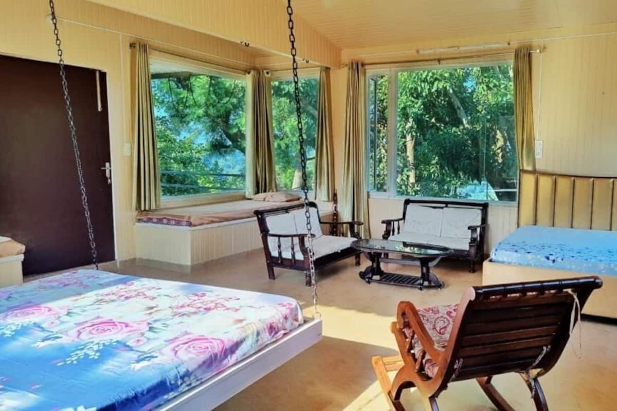 Quarto com duas camas, um sofá, uma poltrona e uma janela com vista para o verde.