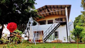 Un bâtiment à deux étages, doté d’un escalier menant à l’étage supérieur, et entouré de verdure.