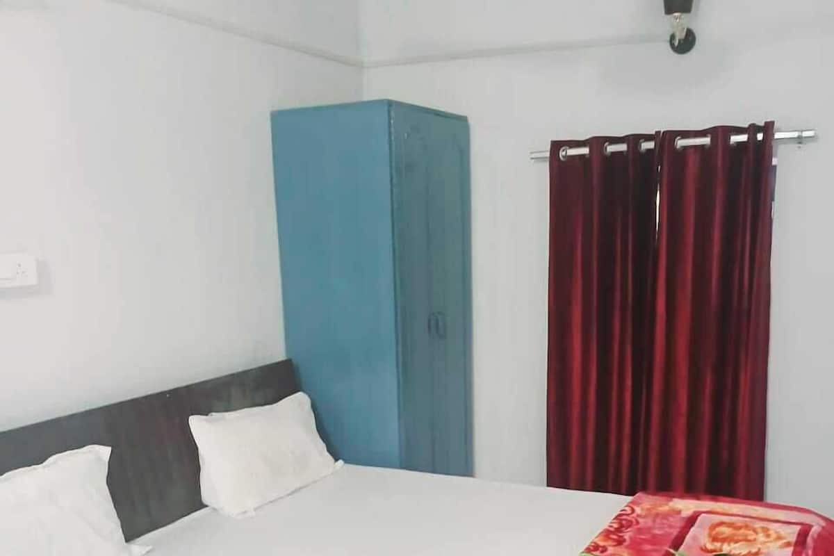 Um quarto com cama, guarda-roupa azul, cortina vermelha e luminária fixada na parede.