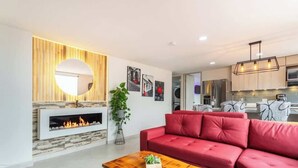 A modern living room with a red sofa, a wooden coffee table, a fireplace, and a kitchen in the background. - Luxe Apartment: By Medellín, Park, Dining, Nightlife, Fast WiFi & Self Check-in (Sabaneta)