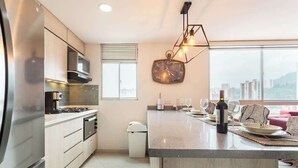 A modern kitchen with a large island, stainless steel appliances, and a city view through large windows. - Luxe Apartment: By Medellín, Park, Dining, Nightlife, Fast WiFi & Self Check-in (Sabaneta)