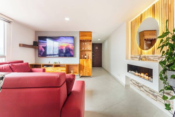 A modern living room with a red sofa, a flat-screen TV, a wooden shelving unit, and a fireplace.