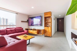A modern living room with a red sofa, a wooden coffee table, a TV mounted on the wall, and a built-in wine rack.