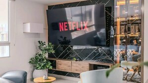 A modern living room with a large flat-screen TV mounted on a wall with a geometric pattern, a wooden cabinet below, and a potted plant to the left.