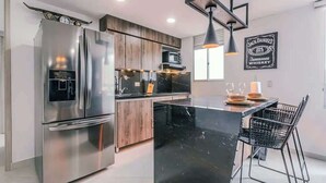 A modern kitchen with a stainless steel refrigerator, wooden cabinets, a black marble island, and a hanging light fixture.