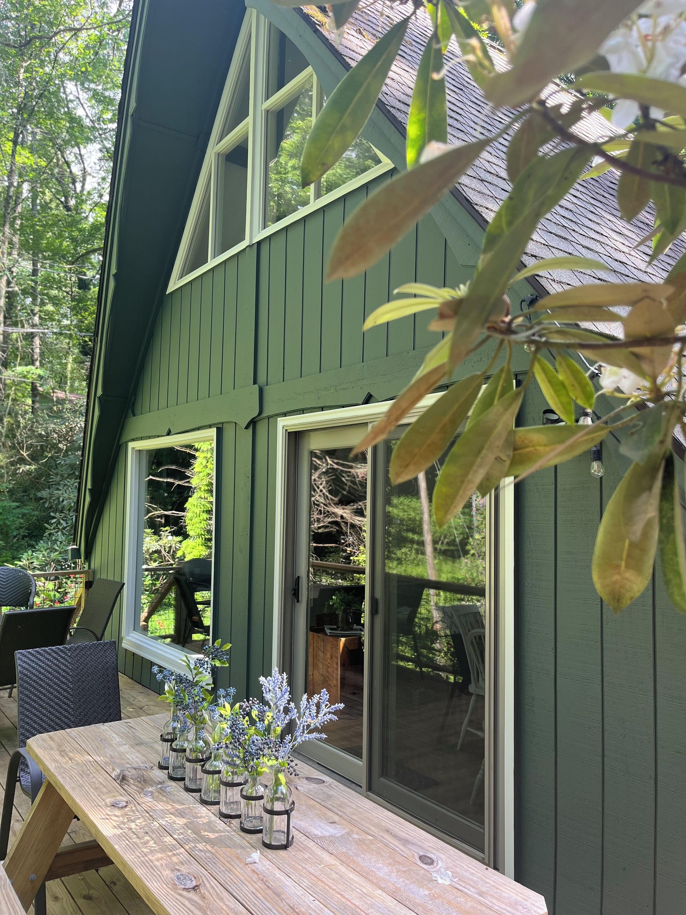 A green house with a wooden deck, a table with glass vases, and a sliding glass door.