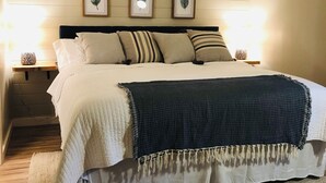 A bedroom with a bed, pillows, a blanket, a rug, and framed leaf artwork on the wall. - Highlands Houses For Rent (Highlands)