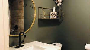 A bathroom with a white sink, a black faucet, a round mirror, and a toilet. - Highlands Houses For Rent (Highlands)