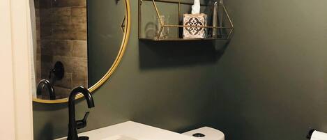 A bathroom with a white sink, a black faucet, a round mirror, and a toilet.