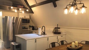 A modern kitchen with a stainless steel refrigerator, a microwave, and a sink. There is a wooden dining table with chairs and a chandelier above. - Highlands Houses For Rent (Highlands)