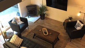 A modern living room with a black leather sofa, two armchairs, a wooden coffee table, and a flat-screen TV mounted on the wall. - Highlands Houses For Rent (Highlands)