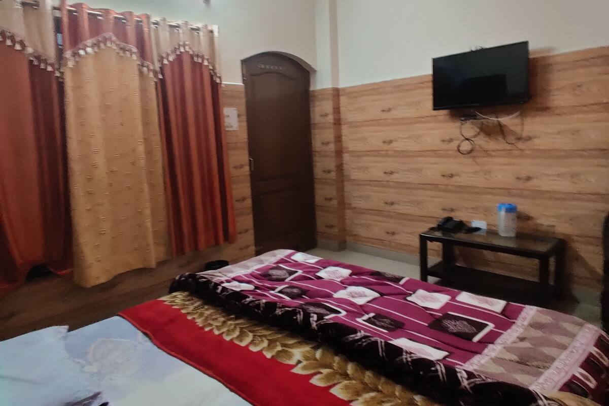 Une chambre à coucher avec un lit, des rideaux, un téléviseur fixé au mur et une petite table.
