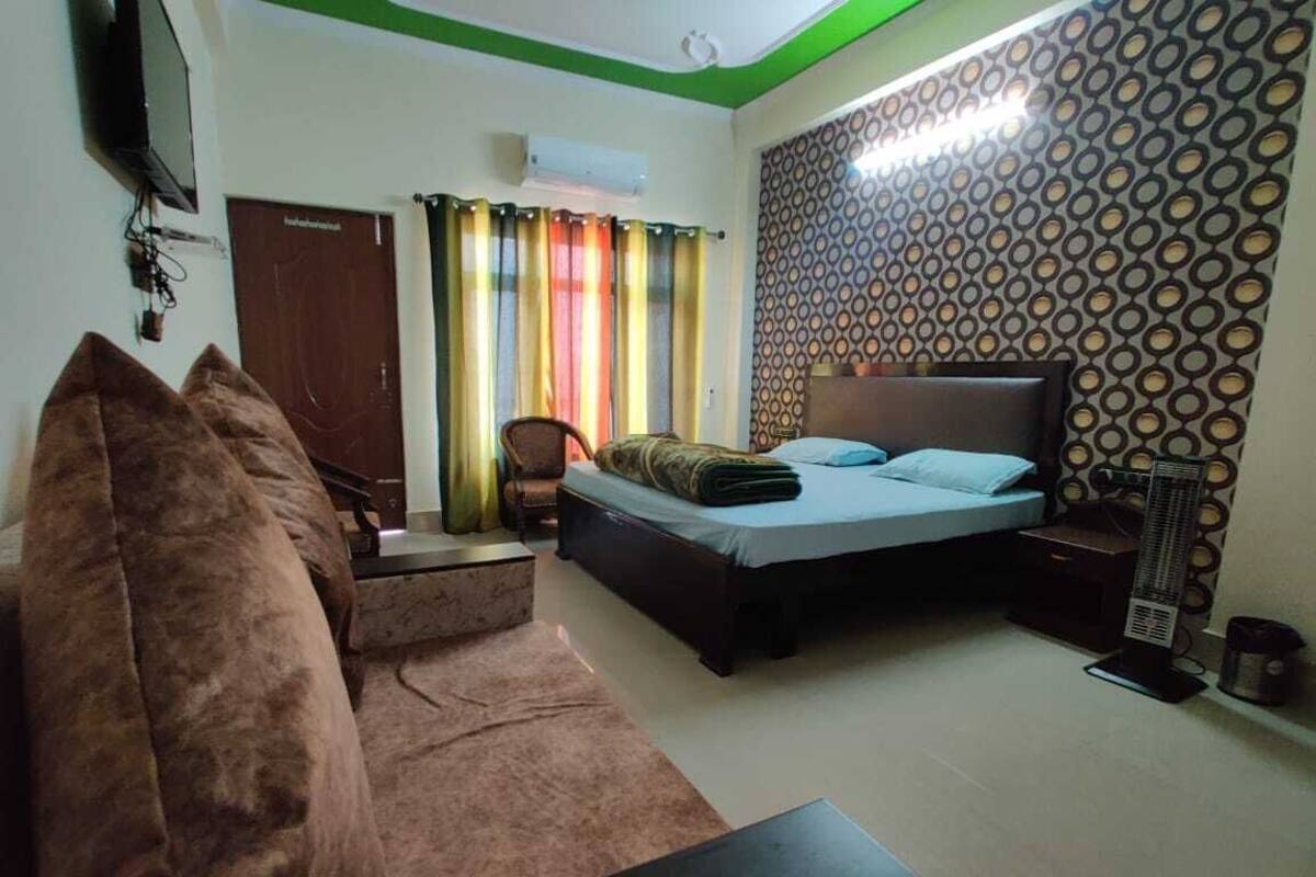 Une chambre avec un lit, un canapé, une chaise, une télévision et un mur décoré d’un motif.