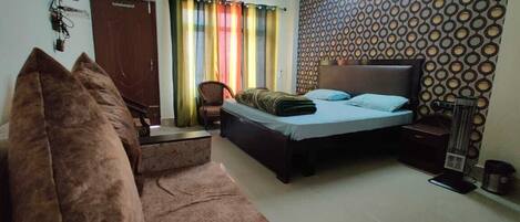 A bedroom with a bed, a sofa, a chair, a TV, and a patterned wall.