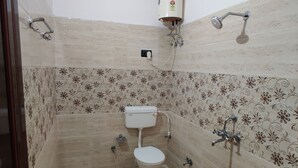 Ein kleines Badezimmer mit Toilette, einem roten Eimer, einem Warmwasserbereiter und einer Dusche.