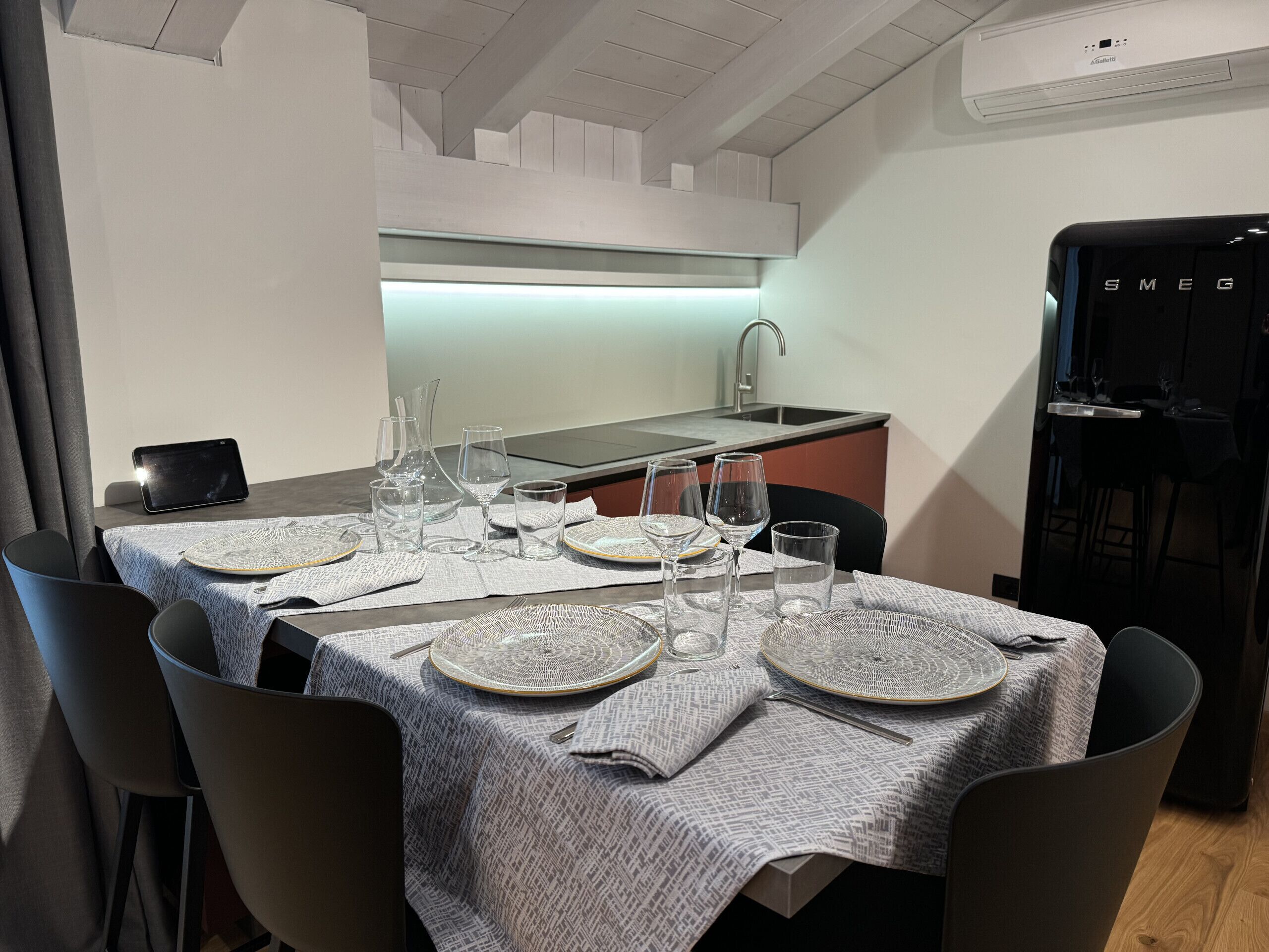 Uma sala de jantar moderna com mesa posta para quatro, cozinha ao fundo e uma geladeira à direita.