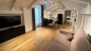 Un appartement moderne de style « loft », avec des poutres apparentes, un coin repas, une cuisine et un salon doté d’un grand téléviseur à écran plat.