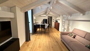 Un appartement moderne de style « loft », avec des poutres apparentes, un coin repas, un canapé et un téléviseur.