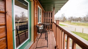 Eine Holzterrasse mit zwei Metallstühlen und einem Tisch, mit Blick auf eine Rasenfläche.