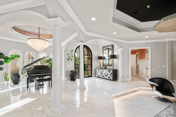 A spacious foyer with a grand piano, a chandelier, and a modern chair.