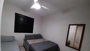 A bedroom with a bed, a desk, a ceiling fan, a window with blinds, and a mirror on the wall. - Round trip - LA04-Bertioga, SESC, Riviera, Vista Linda, Indaiá  (Jardim Rafael Bertioga)