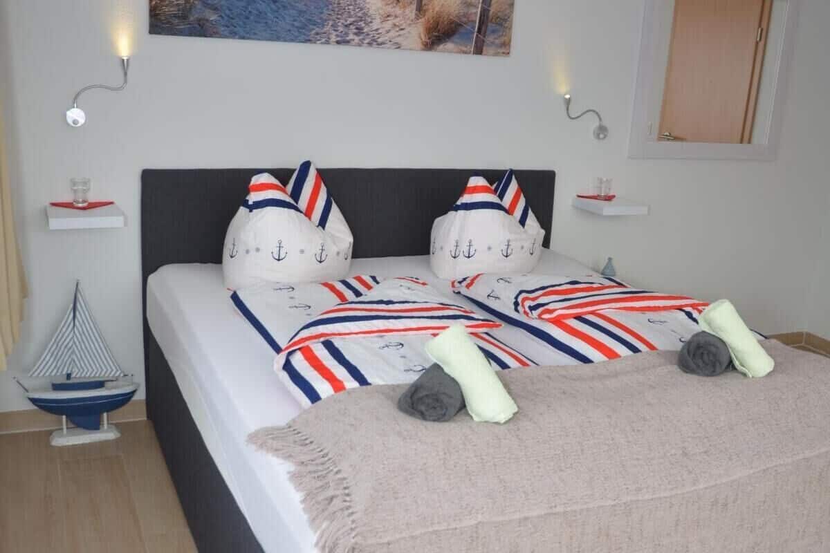 Ein Schlafzimmer mit Bett, einem Bild, einem Nachttisch, einer Lampe und einem kleinen Modell eines Segelbootes.