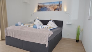 A modern bedroom with a large bed, a painting above the bed, and a potted plant beside the bed. - Gästehaus Meereslust (Cuxhaven)