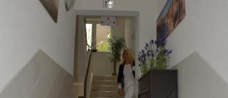 A staircase leading to an upper floor, with a potted plant on the right and a security camera on the wall.