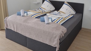 A bedroom with a large bed, a decorative ceiling light, a beach-themed painting, and a bedside table. - Gästehaus Meereslust (Cuxhaven)