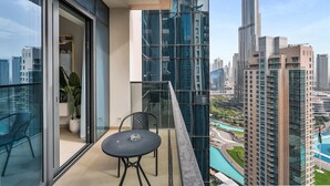 A balcony with a glass railing, a table, and chairs, overlooking a cityscape with high-rise buildings and a swimming pool.