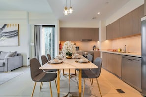 Une cuisine moderne équipée d’appareils électroménagers en acier inoxydable, un coin repas avec une table en marbre et un canapé gris dans le salon.