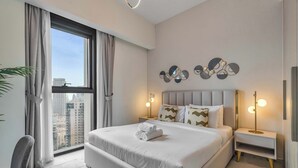 A modern hotel room with a large bed, a desk, a chair, and a view of the cityscape.