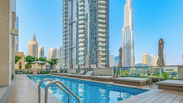 A rooftop pool with a metal railing, surrounded by lounge chairs and umbrellas, with high-rise buildings in the background.