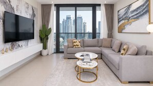 A modern living room with a grey sectional sofa, two round coffee tables, a flat-screen TV, and a large window with a city view.
