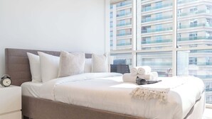 A modern bedroom with a large bed, a nightstand, and a view of a high-rise building.
