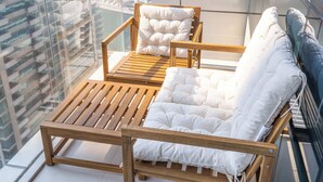 A balcony with two wooden lounge chairs and a cushioned bench, offering a view of a cityscape.