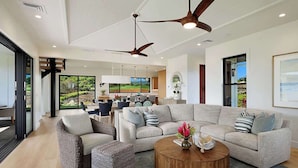 A spacious living area with a large L-shaped sofa, a round coffee table, and a ceiling fan.