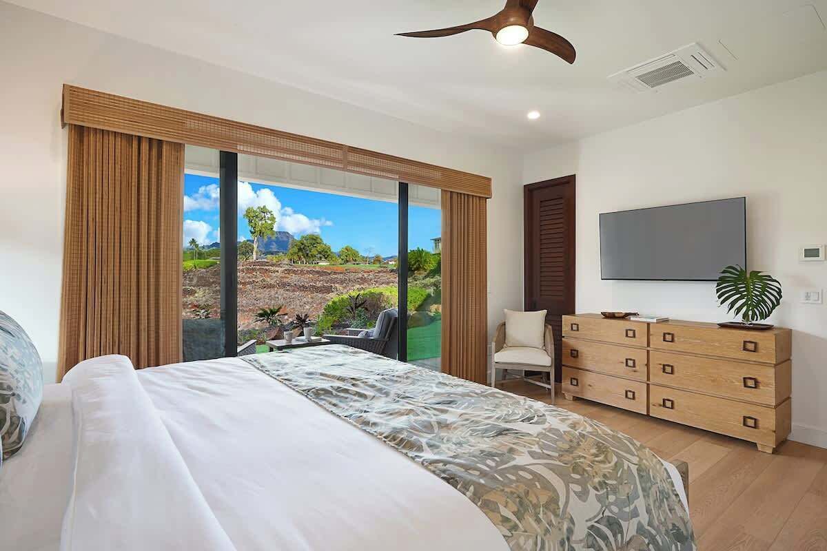 Un dormitorio con una cama grande, un televisor, un aparador y vistas a un paisaje por la ventana.