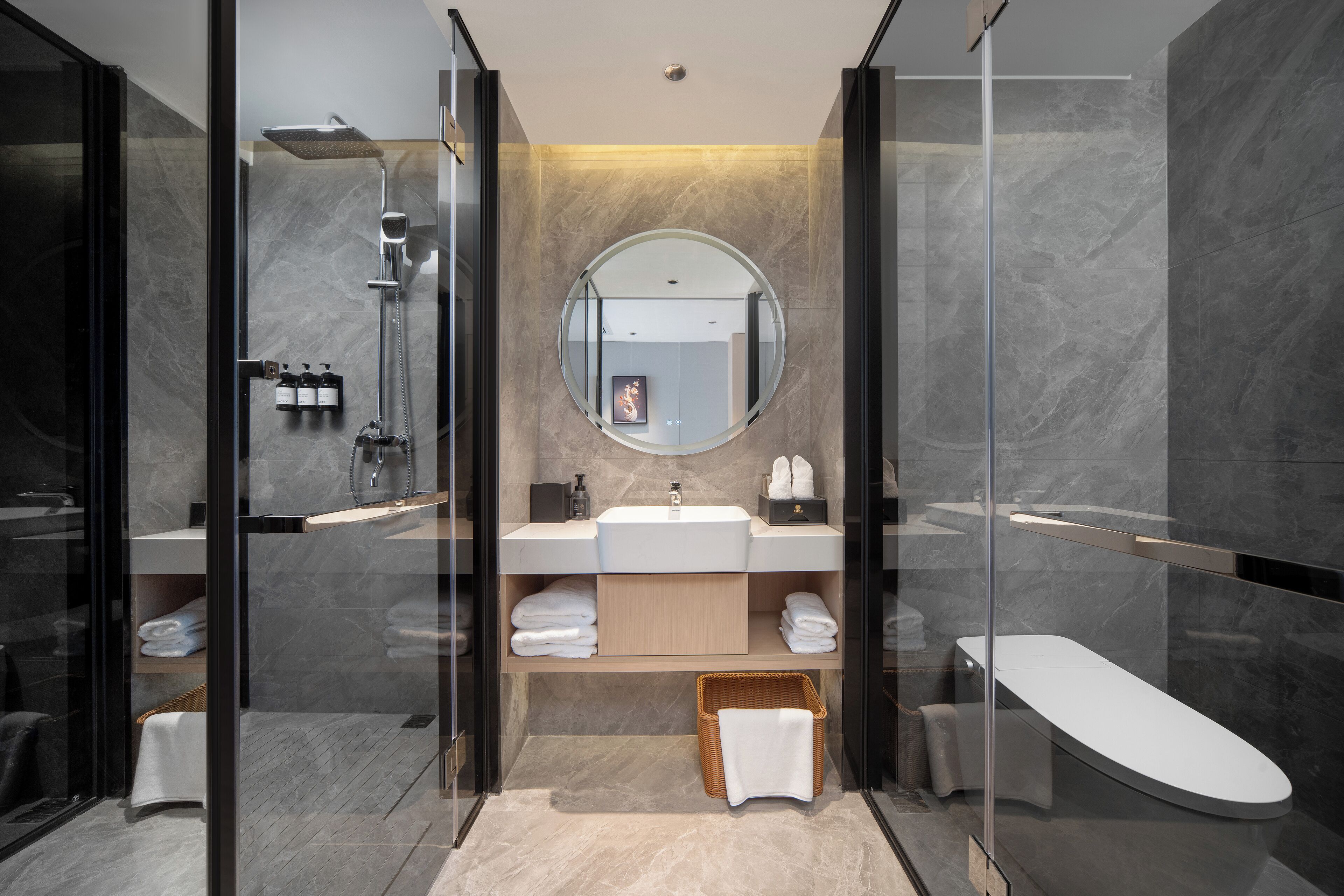 Un baño moderno con ducha envuelta en vidrio, un espejo redondo, un lavabo blanco y una bañera independiente.
