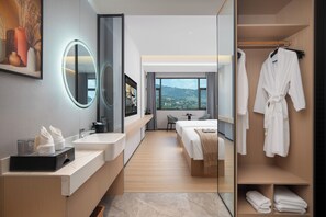 A modern hotel room with a large mirror, a vanity with a sink, a bed, a bedside table, and a view of the outdoors. - JunYa Hotel of Hibiscus town (Xiangxi)
