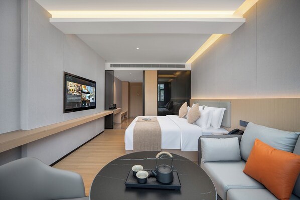 Una habitación de hotel moderna con cama, sofá, mesita de centro con bandeja, televisor montado en la pared y banco de madera.