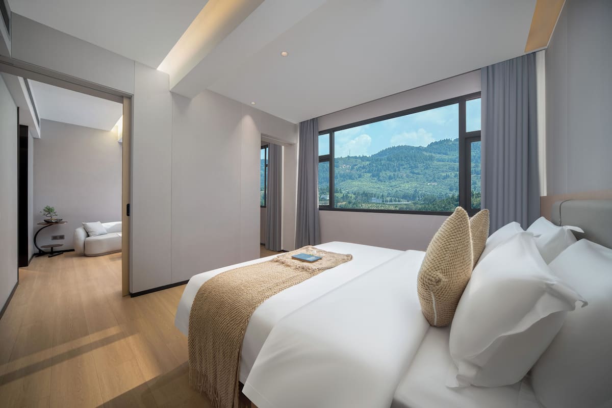 A modern hotel room with a large bed, a view of the outdoors, and a separate seating area.