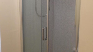 Eine Glastür mit einem Metallgriff, vermutlich zu einem Duschbereich.