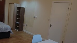 Ein Schlafzimmer mit Bett, Schreibtisch, Stuhl, Kleiderschrank und einer Tür.