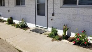 A building with a white textured exterior, a door with a number plate, and small plants and flowers along the front.